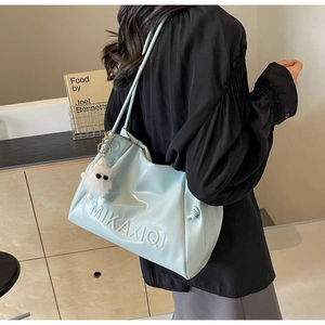 Detail of light blue glossy shoulder bag with embossed letters and a fuzzy monster charm