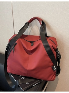 Deep red large capacity travel tote bag with black wide straps on leather sofa