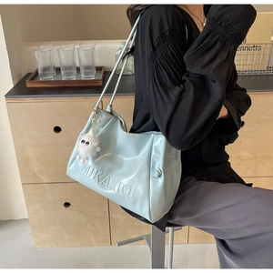 Detail of light blue faux leather tote bag featuring embossed lettering and plush charm