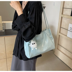 Close-up of light blue glossy shoulder bag with plush monster charm and embossed logo