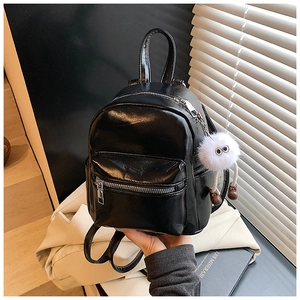 Close-up of black glossy mini backpack with fuzzy plush toy charm and silver zippers