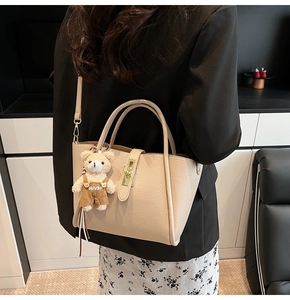 Dettaglio della borsa a secchiello beige in pelle con chiusura in metallo e ciondolo orso