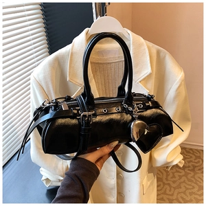 Detalle del bolso cilíndrico negro brillante con hebillas plateadas y dijes de corazón