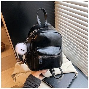 Detail of a shiny black mini backpack with fuzzy charm and smooth PU leather texture