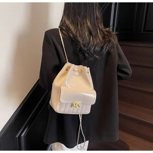 Détail du sac seau crème avec chaîne dorée porté sur une veste de costume noire