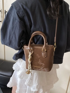 Brown faux leather bucket bag with fashion print and bell charm shown on model