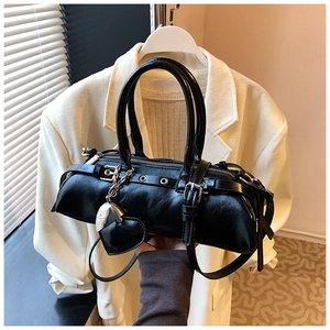 Detalle del bolso tipo almohada de cuero negro con ojales y colgante de corazón alado
