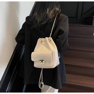 Sac seau crème chic avec bandoulière chaîne et détails dorés porté par un modèle