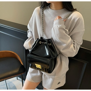 Sac seau noir brillant porté en bandoulière avec boucle dorée et bandoulière chaîne