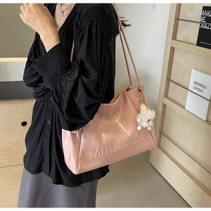 Detail of pink glossy shoulder bag with embossed letters and plush charm accessory