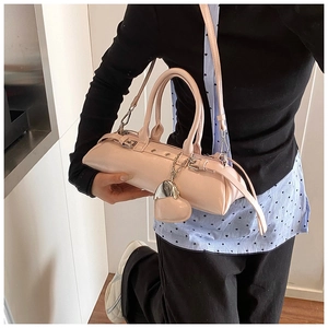 Bolso cilíndrico de cuero rosa con colgante de corazón mostrado en una modelo