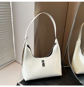 Detail of white glossy crescent bag with silver metallic buckle on dark wood surface