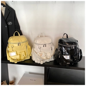 Detailed view of glossy leather backpacks in yellow, beige and black with multi-pockets