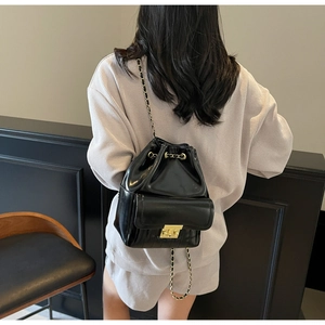 Détail du sac seau noir brillant avec chaîne dorée et boucle sur une tenue beige