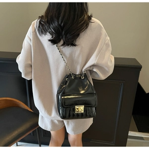 Sac seau noir brillant avec bandoulière chaîne porté par un mannequin en intérieur