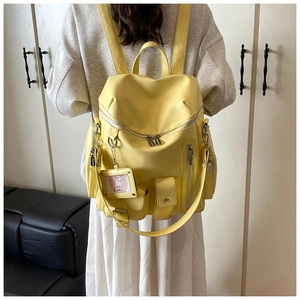 Detail of yellow PU leather backpack with multiple pockets and silver hardware on model