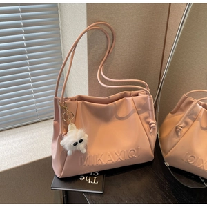 Detail of pink PU leather shoulder bag with embossed logo and cute plush monster charm