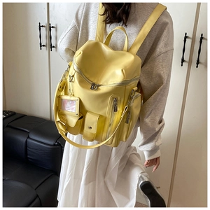 On-model view of bright yellow leather backpack with multiple pockets and transparent charm