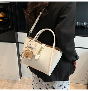 Dettaglio borsa in pelle crema grana litchi con chiusura dorata e ciondolo a forma di orso