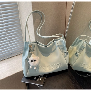 Close-up of light blue leather shoulder bag with logo embossing and a plush monster charm