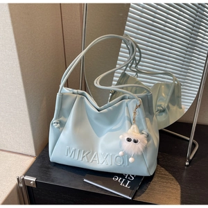 Detail of light blue faux leather handbag with embossed letters and white plush charm
