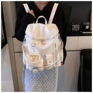 Detail of a creamy white glossy leather backpack with multi-pocket design and bear charm
