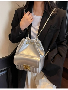 Sac seau en similicuir argenté avec chaîne dorée porté par un mannequin en intérieur