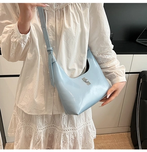 Close-up of ice blue patent leather crescent bag with silver buckle on a model