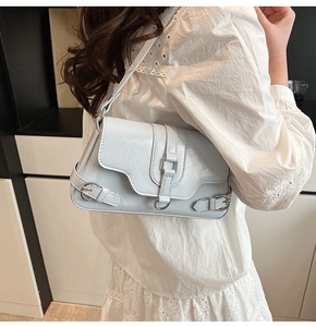 Gros plan d'un sac sous le bras en cuir crème avec boucles métalliques porté par un mannequin