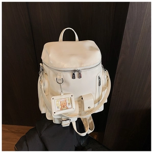 Detail of cream white leather backpack with multiple pockets and cute bear charm