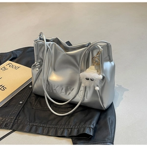 Metallic silver tote bag with embossed letters and a white plush monster charm detail