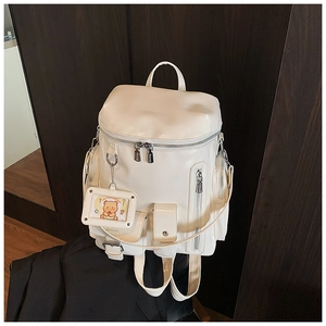 Detail of cream PU leather backpack with silver zippers and a cute bear card holder