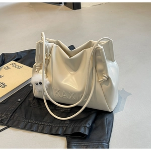 Detail of a creamy white drawstring handbag with a cute plush monster charm on a black coat