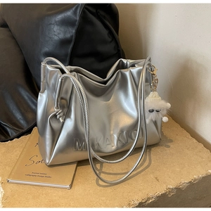 Close-up of metallic silver pleated shoulder bag with MKAXIC logo and plush monster charm