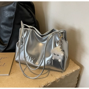 Detail of silver metallic tote with embossed logo and fuzzy monster charm on stone