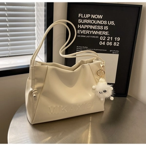 Close-up of cream shoulder bag with embossed texture and plush monster charm decoration