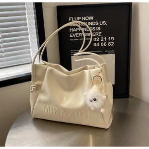 Close-up of pleated cream shoulder bag with plush charm and embossed logo detail