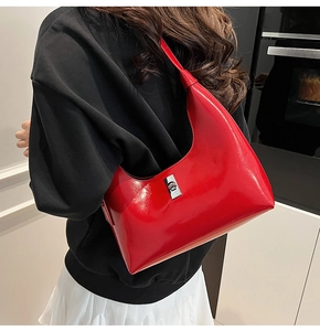 Polished red patent leather crescent hobo bag with silver buckle worn on shoulder