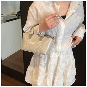 Detailed close-up of cream-colored glossy leather handbag with metallic square buckles