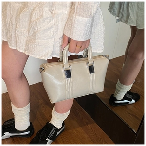Detailed view of a light beige leather handbag featuring silver hardware and a top zipper