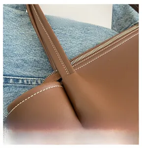 Macro view of brown leather tote bag with white contrast stitching and metal zipper detail