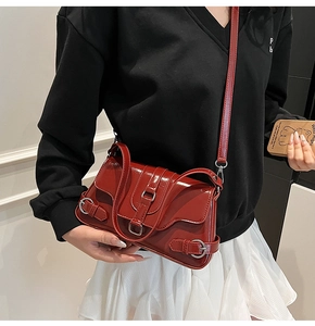 Détail de la finition en cuir verni rouge foncé et boucles argentées sur le sac bandoulière