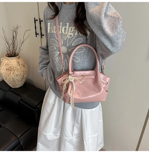 Detail der hellrosa Handtasche aus Lackleder mit Schleifenanhänger und Flügeldesign