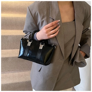 Close-up of black glossy handbag with silver metal buckle on a dark grey blazer outfit