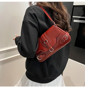 Détail du sac à bandoulière rouge brillant avec boucles porté sur un pull noir