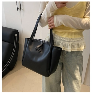 Detail of black faux leather tote bag with white contrast stitching and zip closure