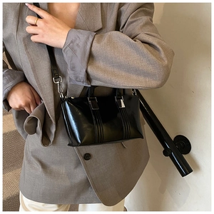 Model wearing high-gloss black patent leather handbag with silver metallic buckles