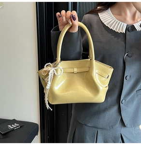 Detail der hellgelben glänzenden Handtasche mit Perlenspitzenanhänger und Metallschnalle