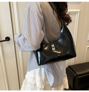 Side view of black glossy patent leather crescent shoulder bag with silver buckle worn by model