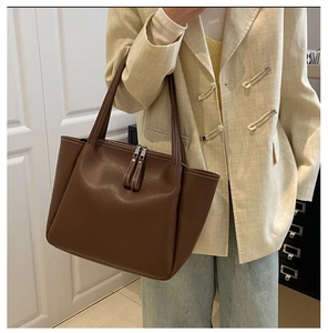 Close-up of deep brown leather tote bag with white contrast stitching and long zipper pulls